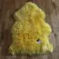 A bright yellow sheepskin rug with a thick, textured wool pile in a natural pelt shape.