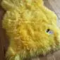 A bright yellow sheepskin rug with long, thick wool and a natural hide shape.