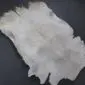 Natural goatskin rug with light grey and white mottled fur in an irregular organic shape.
