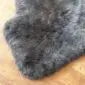 Sheepskin-Double-Grey-b Close-up of a thick, dark grey sheepskin rug with a natural textured wool pile on a wooden floor.