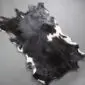 Natural goatskin rug with black and white mottled fur and irregular edges.