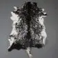 Natural goatskin rug with long black and white mottled fur and an irregular shape.