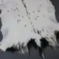 Natural white goatskin rug with black spots and a dark grey border.