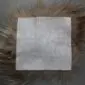 Underside of a square taupe Icelandic sheepskin seat pad showing the grey suede backing and long natural wool fringe.
