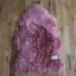 A natural-shaped pink sheepskin rug with thick, textured wool pile on a wooden floor.