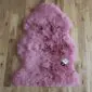 A dusty pink sheepskin rug with thick, curly wool and a natural pelt shape on a wooden floor.