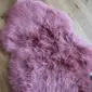 A fluffy, dusty pink sheepskin rug with a natural, irregular shape and long wool fibres.
