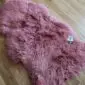 A fluffy, long-pile pink sheepskin rug with an irregular natural shape on a wooden floor.