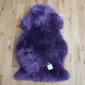 A fluffy, purple sheepskin rug with an irregular natural shape, laid flat on a light wood floor.