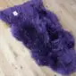 A deep purple sheepskin rug with long, thick wool and a natural, irregular shape.