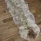 Long double sheepskin rug with natural cream, grey, and brown mottled wool on a wooden floor.