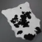 Natural white calfskin rug with irregular black spots and patches, shown from an overhead perspective.