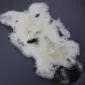 Irregularly shaped cream sheepskin rug with dark brown and black spots and a large dark patch at one end.