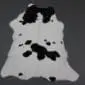 Natural calfskin rug with a white base and irregular black spots, shown from above on a dark grey background.