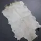 Natural goatskin rug in off-white and cream tones with an irregular shape and short hair texture.