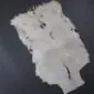 Natural white goatskin rug with irregular edges and short hair texture on a dark grey background.