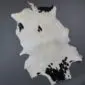 Natural goatskin rug with an irregular shape featuring white fur and black spotted markings.