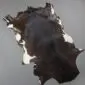 Natural goatskin rug with dark brown and black fur featuring white patches along the edges.