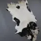 Natural goatskin rug with white fur and large black patches, displayed on a grey background.