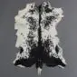 Natural goatskin rug with a speckled black and white pattern and irregular edges on a grey background.