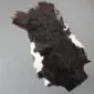 Natural goatskin rug with long, textured dark brown and black fur featuring white patches along the edges.