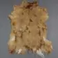Natural goatskin rug with tan and light brown fur, irregular edges, and white patches at the base.