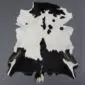 Natural goatskin rug with a black and white spotted pattern and irregular edges on a grey background.