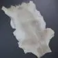 Natural goatskin rug with cream and light brown mottled fur in an irregular hide shape.