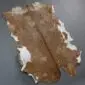 Natural goatskin rug with brown and tan mottled patterns and white edges.
