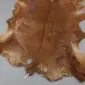 Natural goatskin rug with mottled brown and tan fur, featuring irregular edges and a central spine marking.