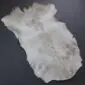 Natural goatskin rug with white and grey mottled fur in an irregular shape.