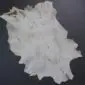 Natural goatskin rug with cream and grey fur in an irregular shape.