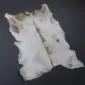 Natural goatskin rug with white, grey and light brown markings and an irregular shape.