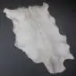 Natural white goatskin rug with grey and tan markings and an irregular shape on a dark grey background.