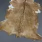 Natural goatskin rug with tan and light brown fur, featuring white patches and a dark dorsal stripe.