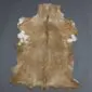 Natural goatskin rug with mottled tan, brown and white fur, featuring a dark dorsal stripe and irregular edges.