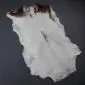 Natural goatskin rug with white fur and dark brown markings at the top edge, shown .