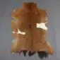 Natural goatskin rug with tan and brown fur, featuring white patches and dark edges on a grey background.