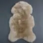 Natural beige sheepskin rug with a thick, textured wool pile and an irregular organic shape.
