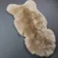 Natural beige sheepskin rug with a thick, fluffy texture and an irregular organic shape on a dark grey surface.