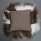 Reverse side of a square Icelandic sheepskin cushion showing brown fabric backing and long spotted rusty wool trim.