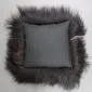 Reverse side of a square grey cushion with a long, dark shaggy sheepskin trim.