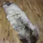 Long double sheepskin rug with thick cream and grey mottled wool on a wooden floor.