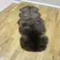 Long double sheepskin rug with thick, dark brown and grey mottled wool on a wooden floor. detail view