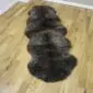 Long double sheepskin rug with thick, dark brown and grey mottled wool on a wooden floor.