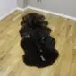 Long double sheepskin rug with thick dark brown and black wool in a natural curved shape.